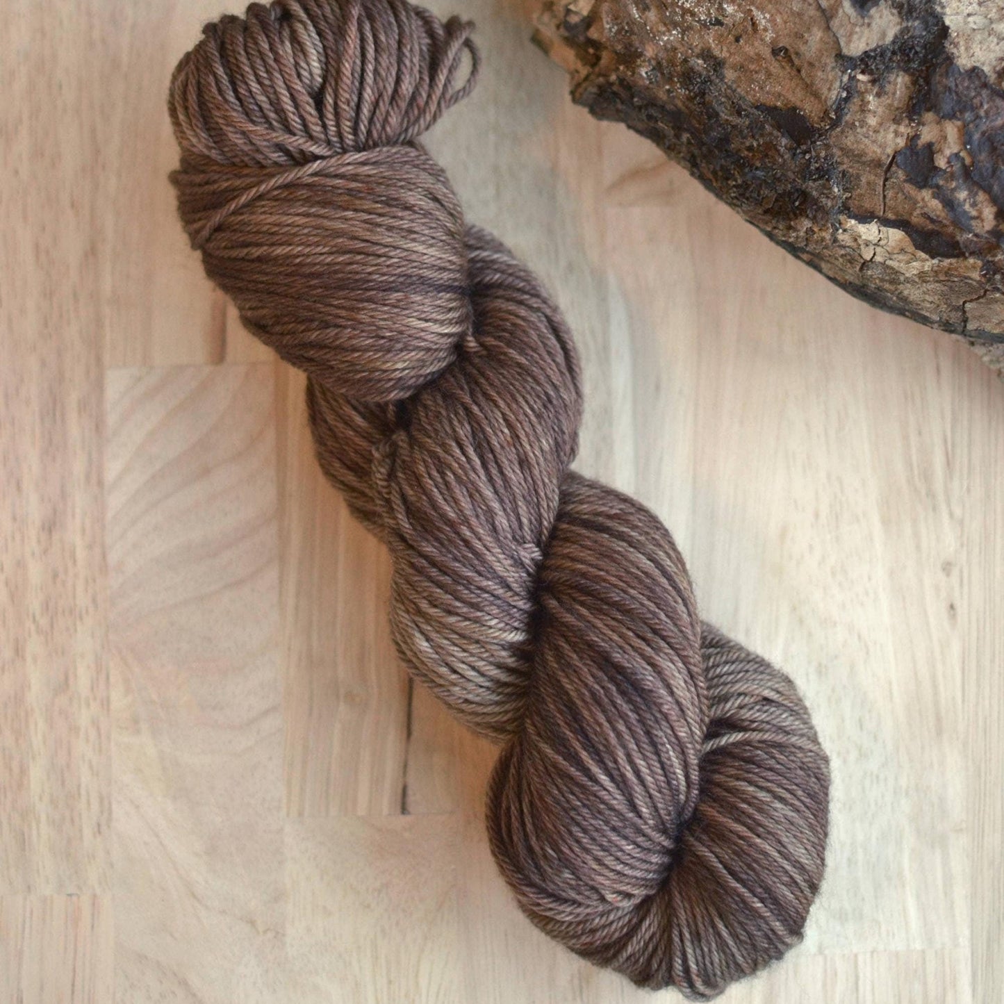 Neutral brown hand dyed merino wool yarn arranged on a wooden backdrop.