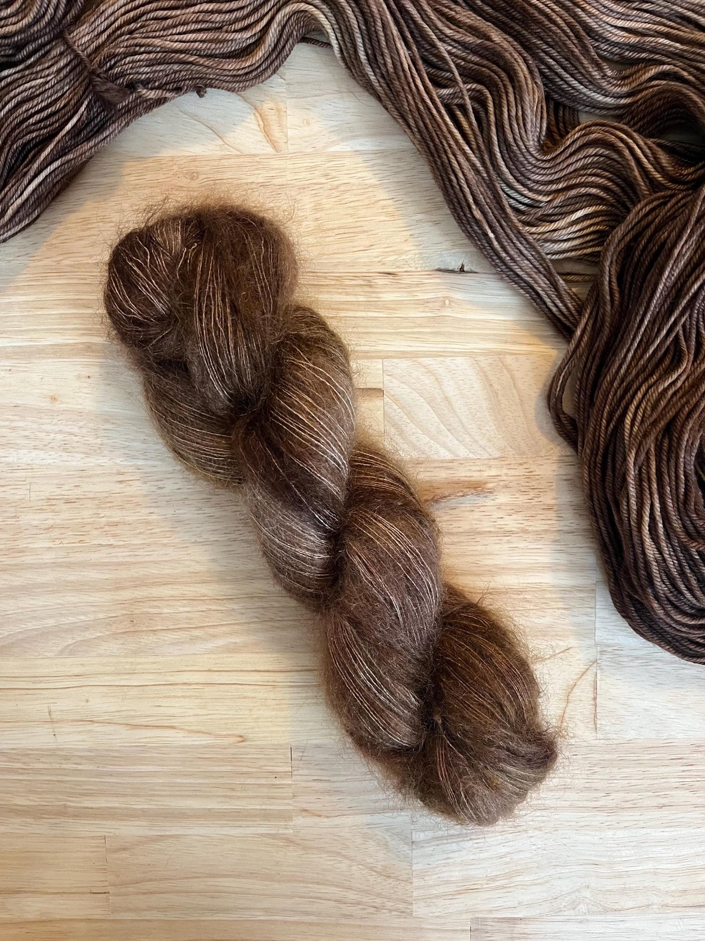 Hand dyed variegated neutral brown mohair silk yarn arranged on a wooden backdrop.