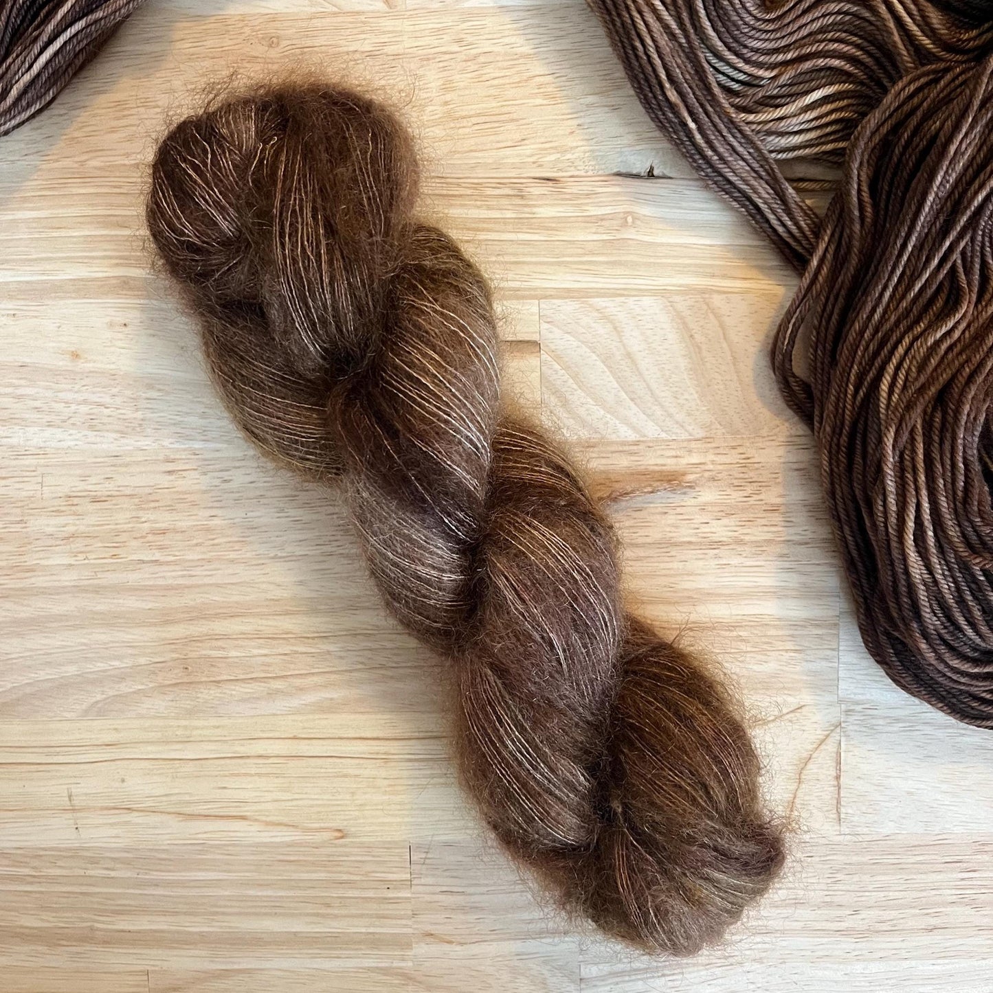 Hand dyed variegated neutral brown mohair silk yarn arranged on a wooden backdrop.