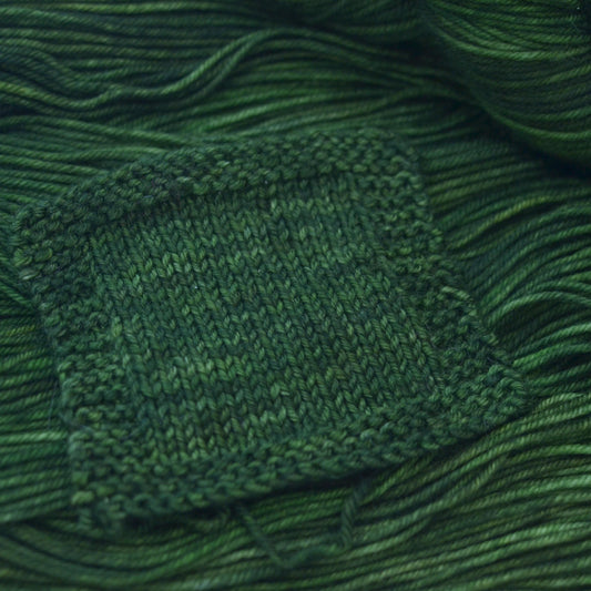 A knit swatch of hand dyed variegated green merino wool yarn.