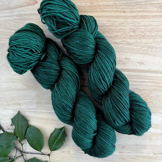 Skeins of hand dyed dark forest green merino wool yarn.