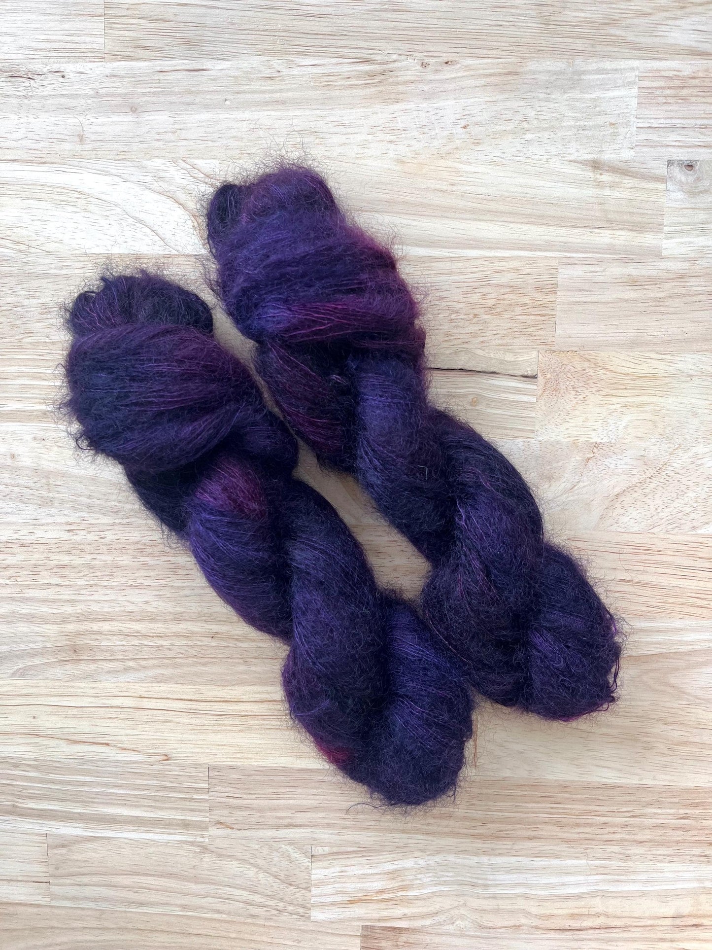 Two skeins of hand dyed variegated purple and dark red mohair silk lace yarn.