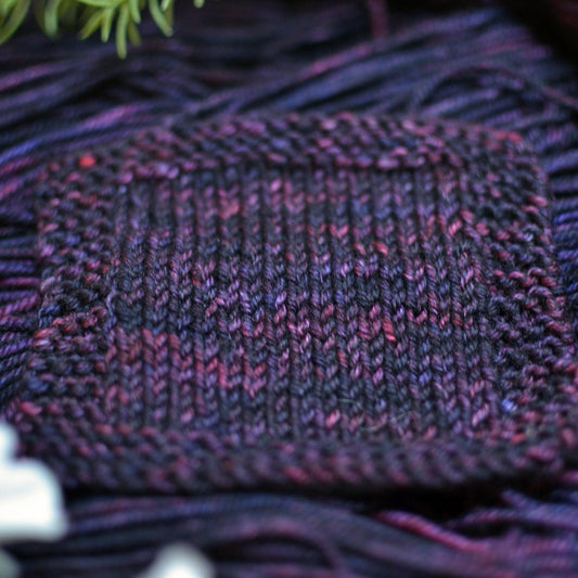 A knit swatch of variegated purple hand dyed yarn.