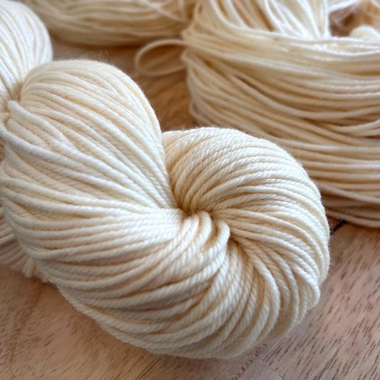 A skein of cream colored wool yarn against a wood background.