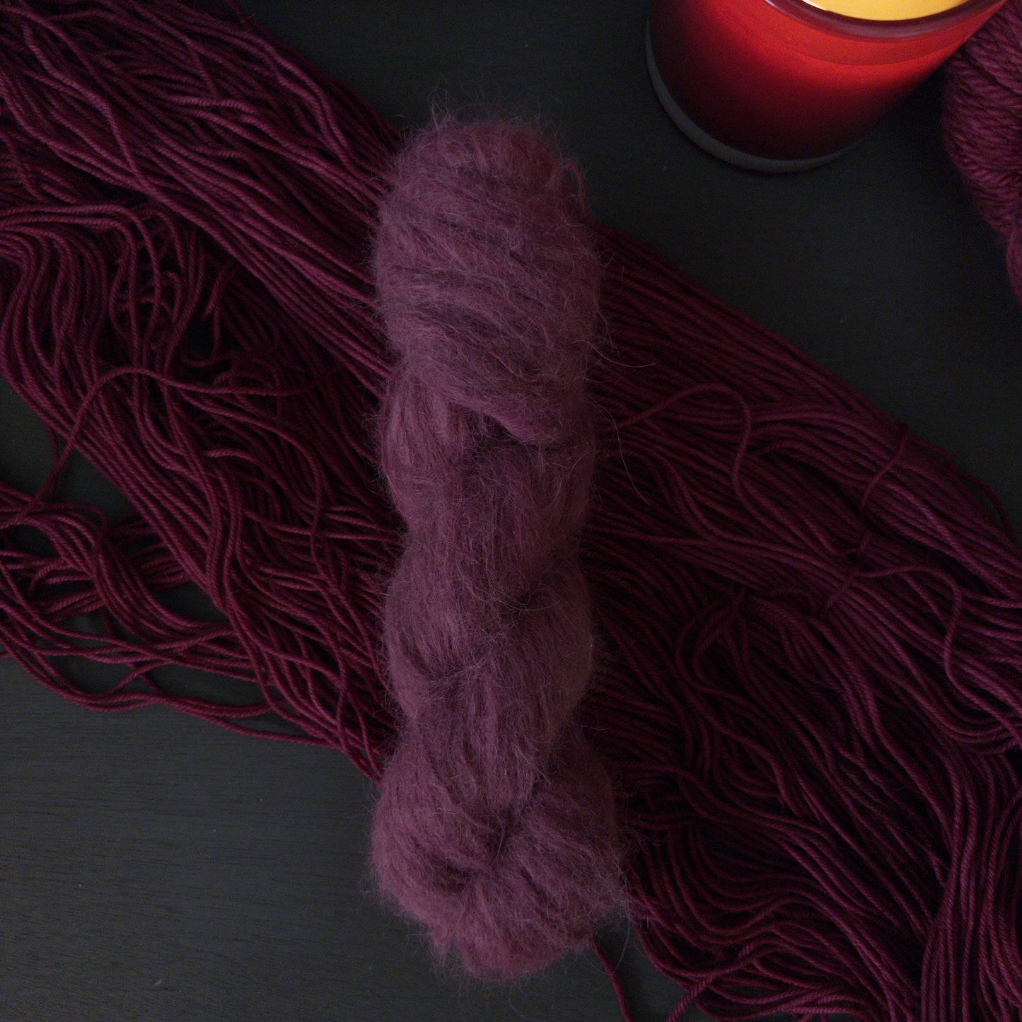 Burgundy yarn skeins and a lit candle on a dark surface
