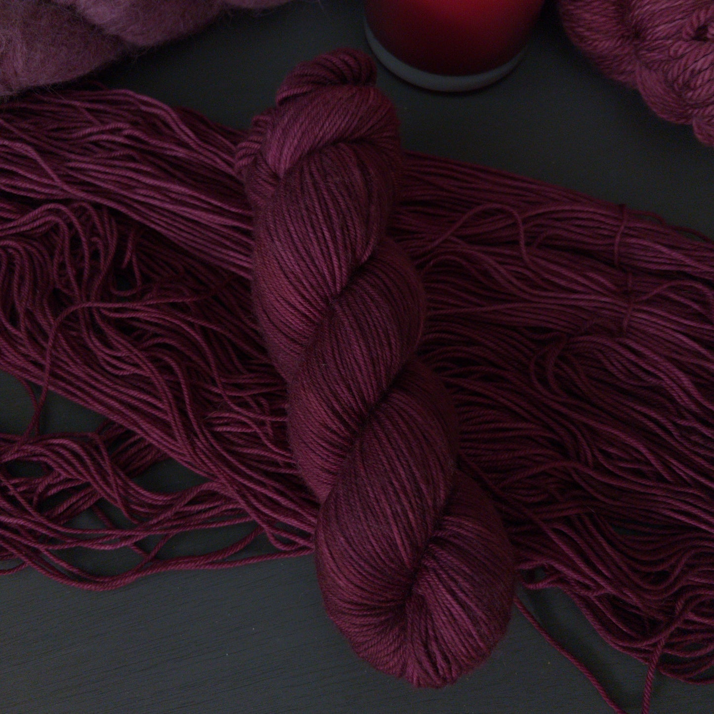 Burgundy yarn skeins with a lit red candle on a dark surface