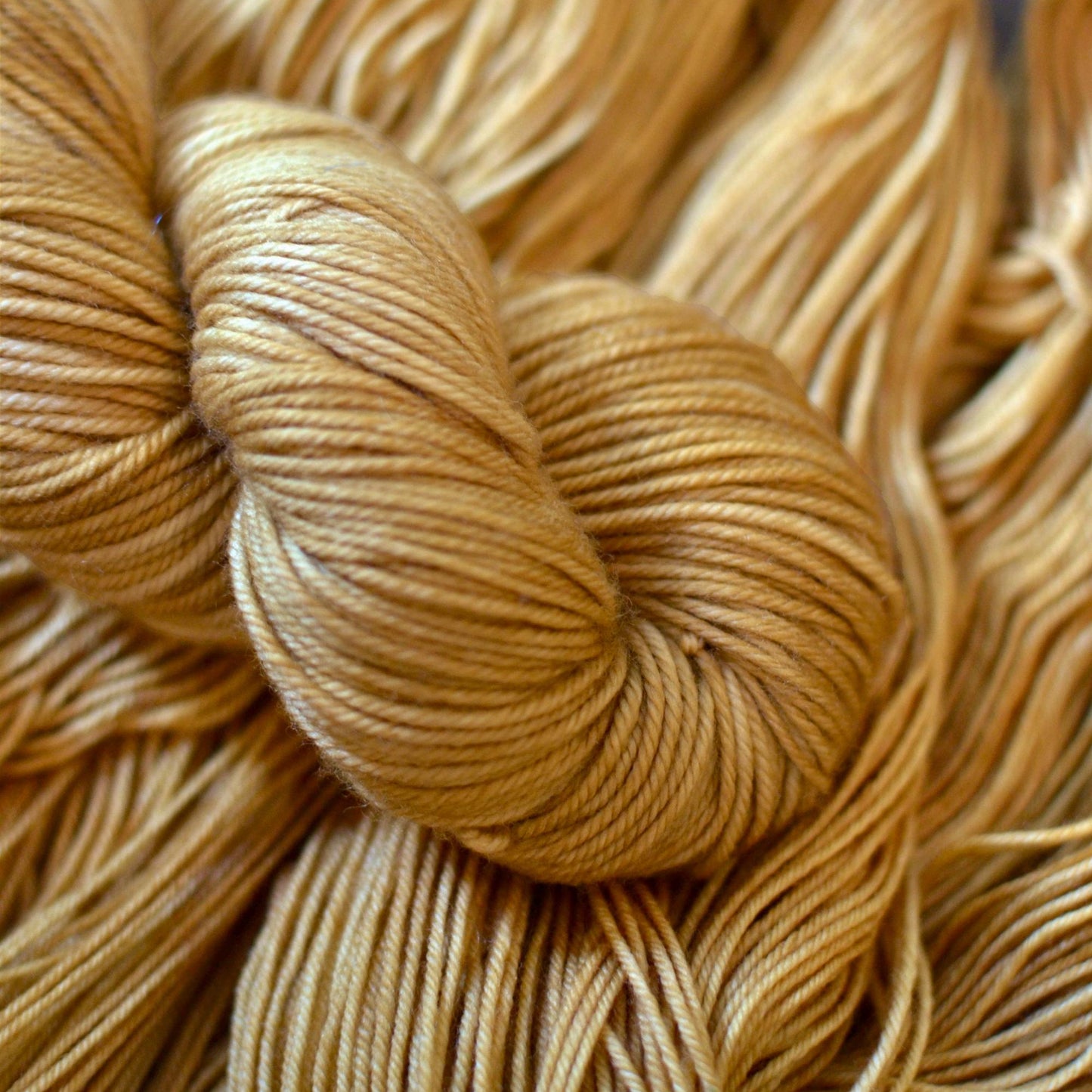A skein of hand dyed caramel colored yarn arranged against more yarn.