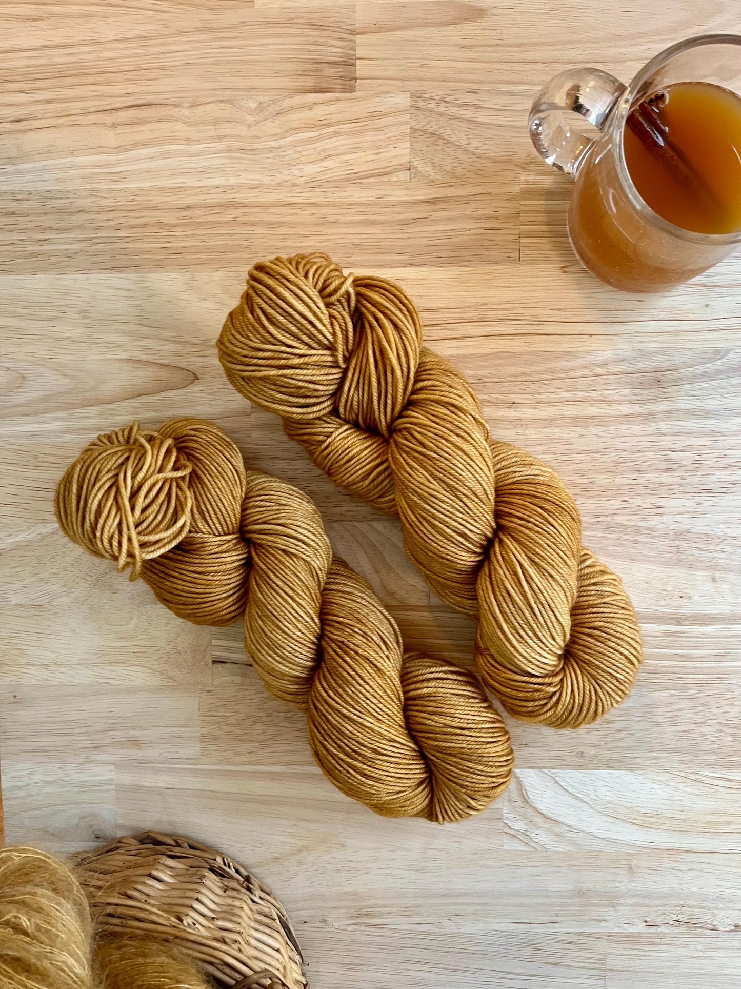 Two skeins of golden tan colored hand dyed wool yarn against a wood background.