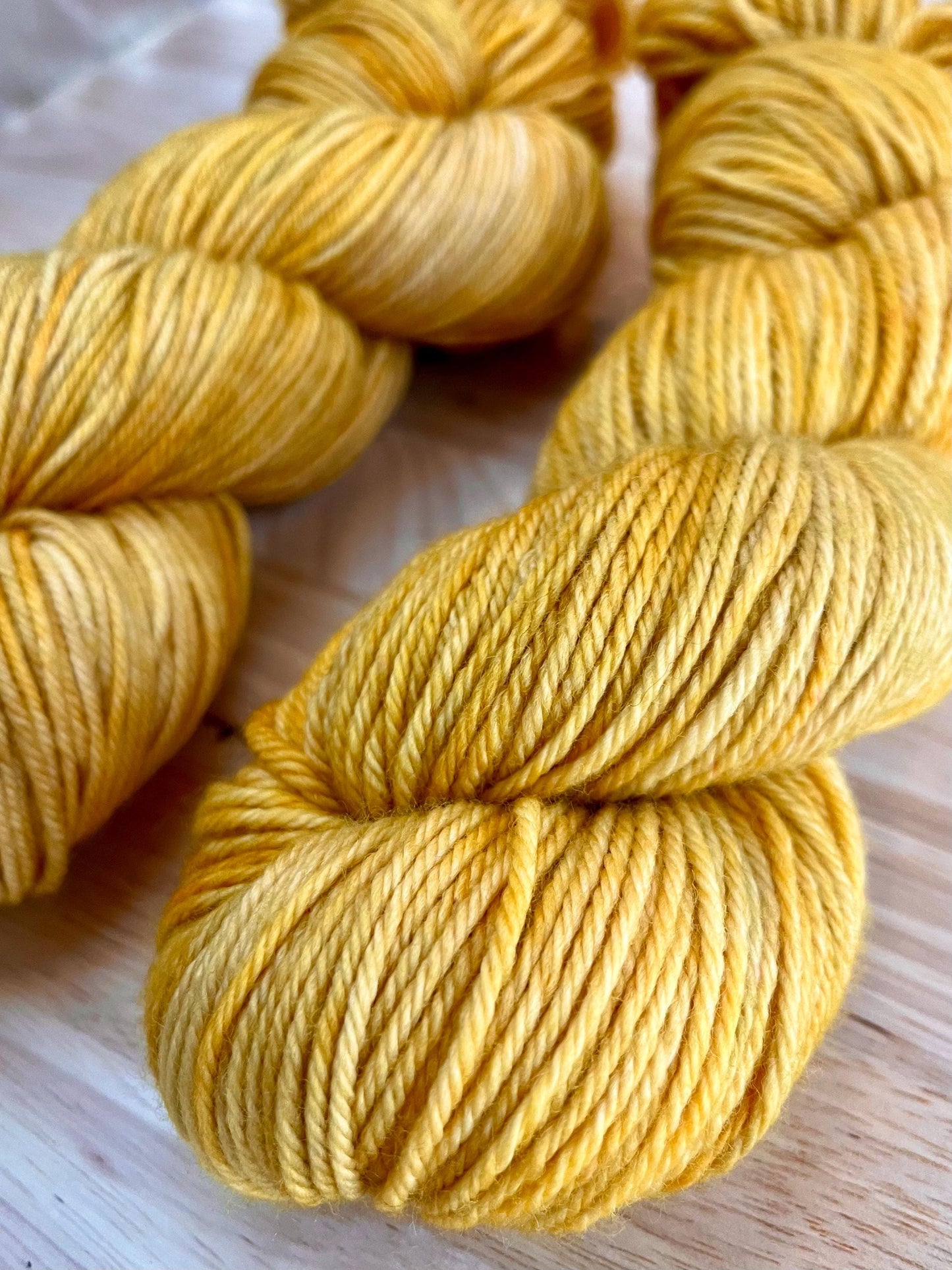 Two skeins of worsted weight hand dyed variegated yellow and gold wool yarn.