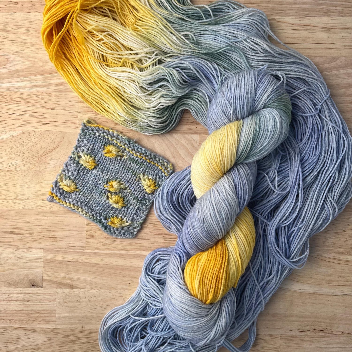 A skein and knit swatch of pale blue and yellow hand dyed merino wool yarn designed for assigned pooling.
