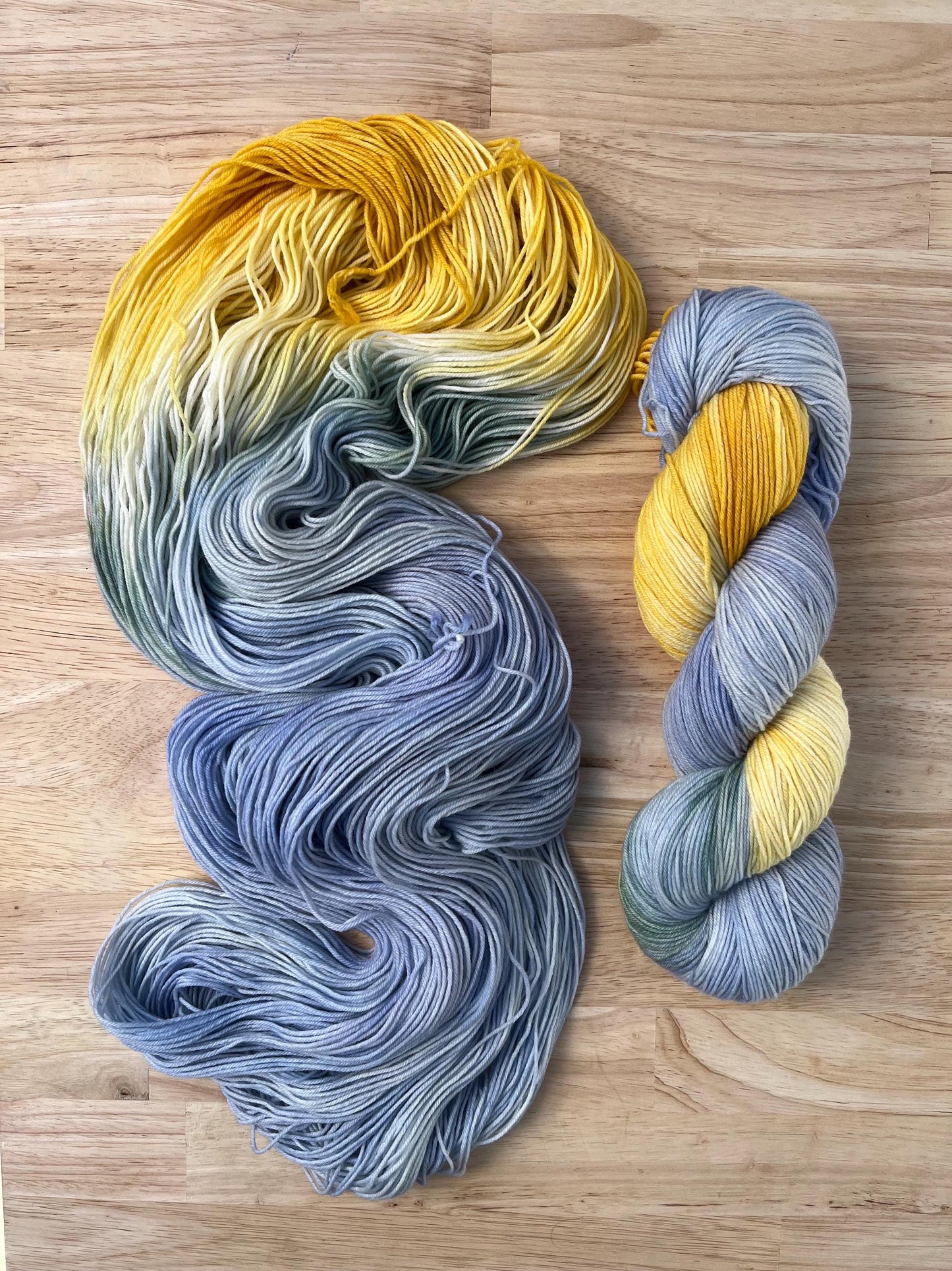 Two skeins of pale blue and yellow hand dyed merino wool yarn designed for assigned pooling.