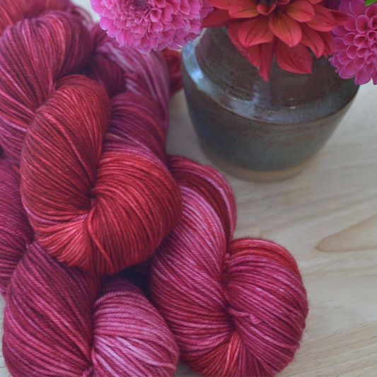 Red and pink yarn skeins with a vase of flowers on a wooden surface