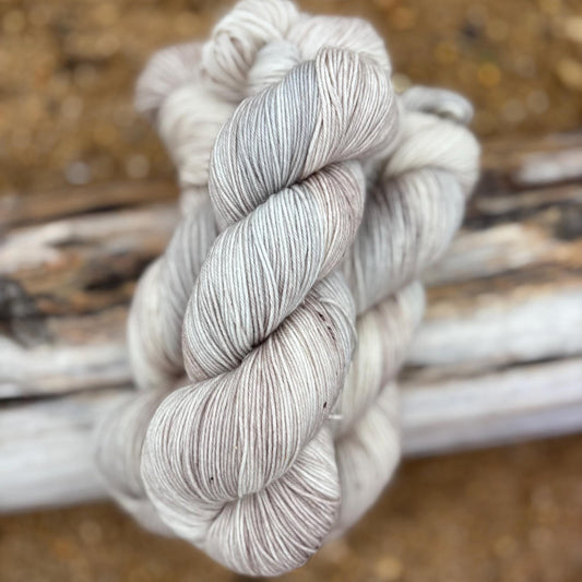 Skeins of hand dyed pale gray and beige yarn arranged n a piece of driftwod.