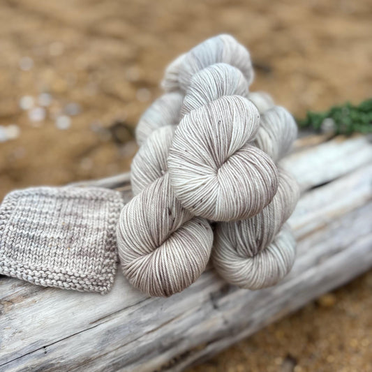 Skeins of hand dyed pale gray and beige yarn arranged on a piece of driftwood.