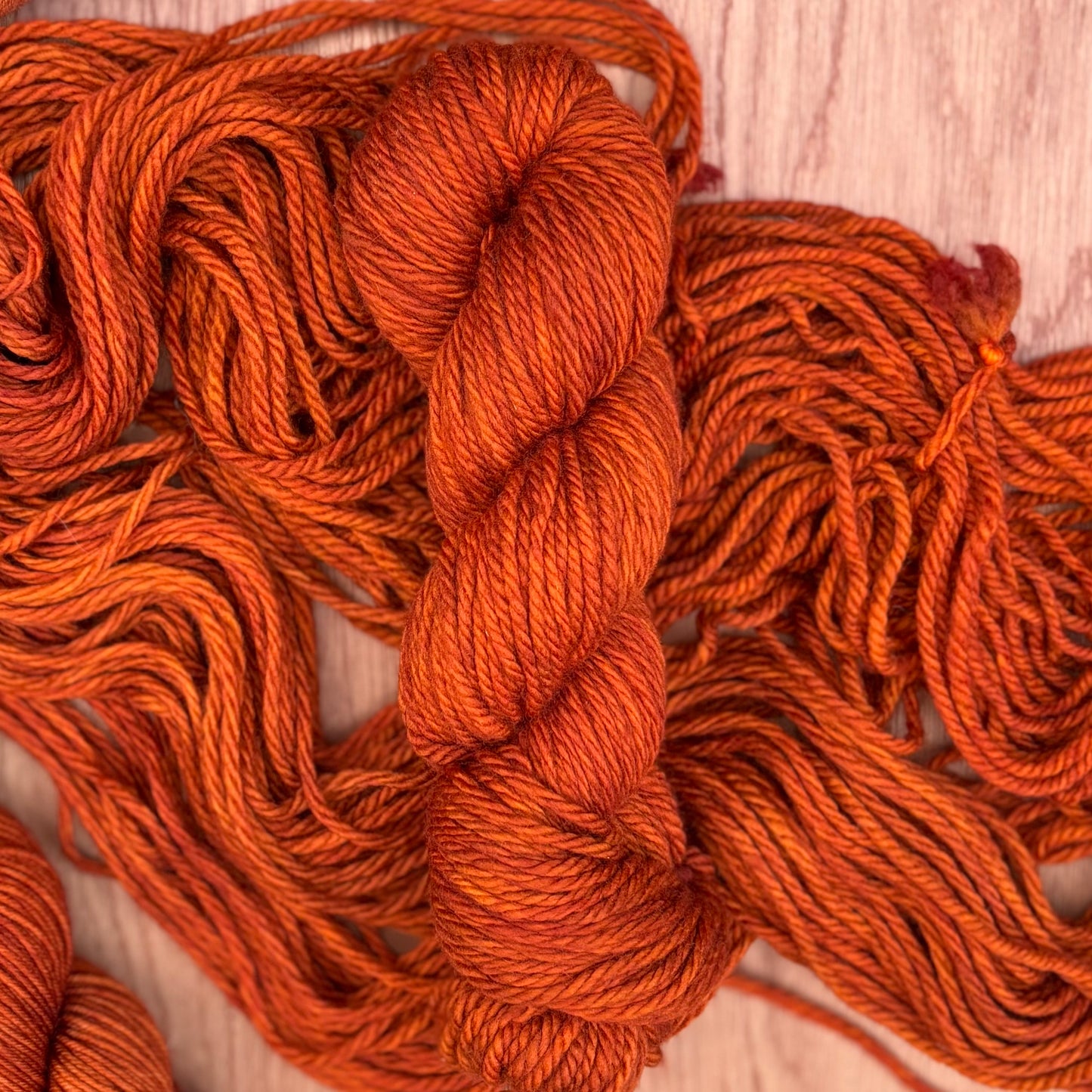 Two skeins of hand dyed orange yarn on a wooden surface