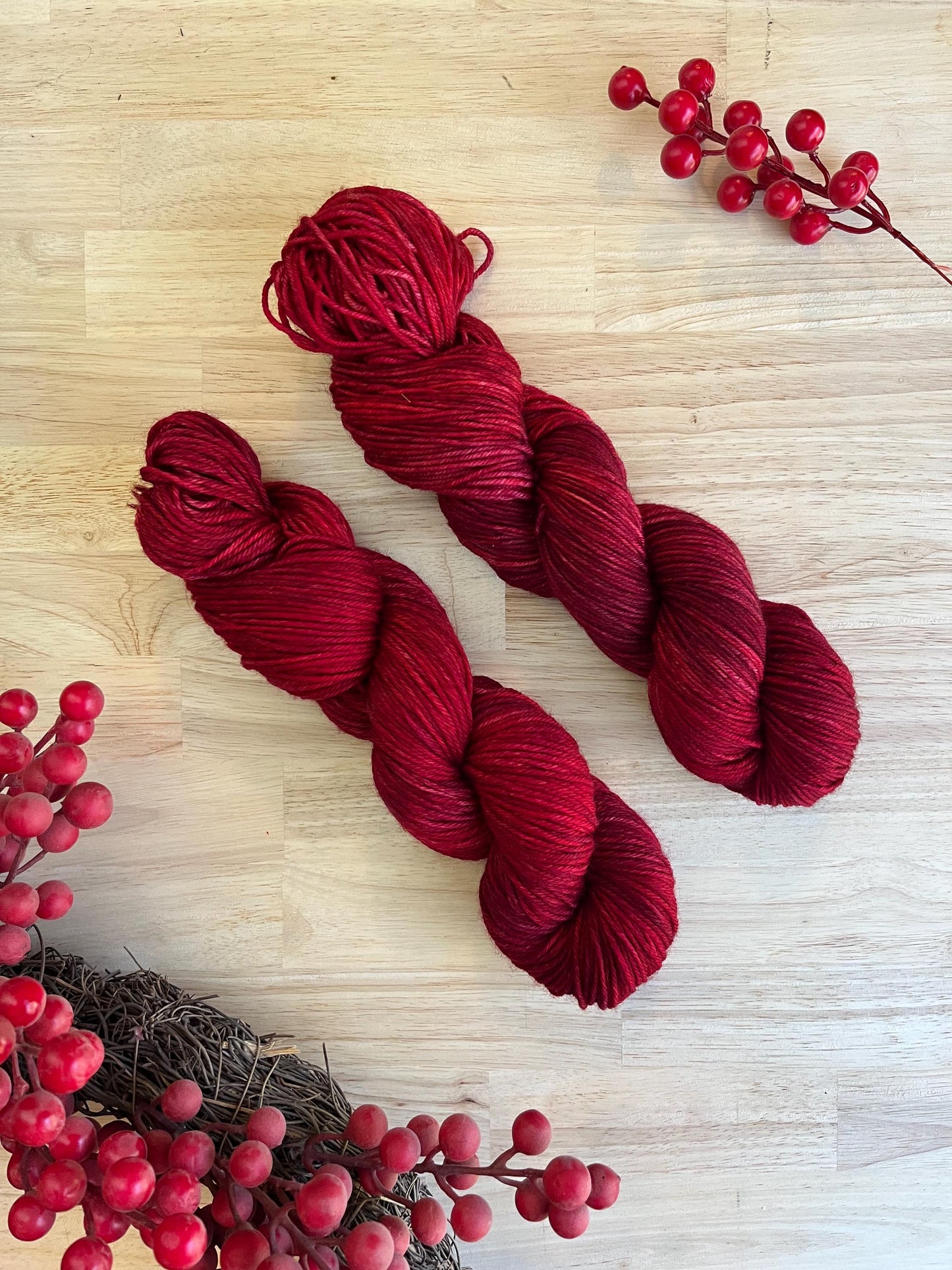 Two skeins of hand dyed red merino wool yarn arranged on a wood background.