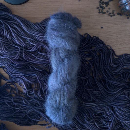 Gray skein of yarn on a wooden surface with more yarn and black objects in the background
