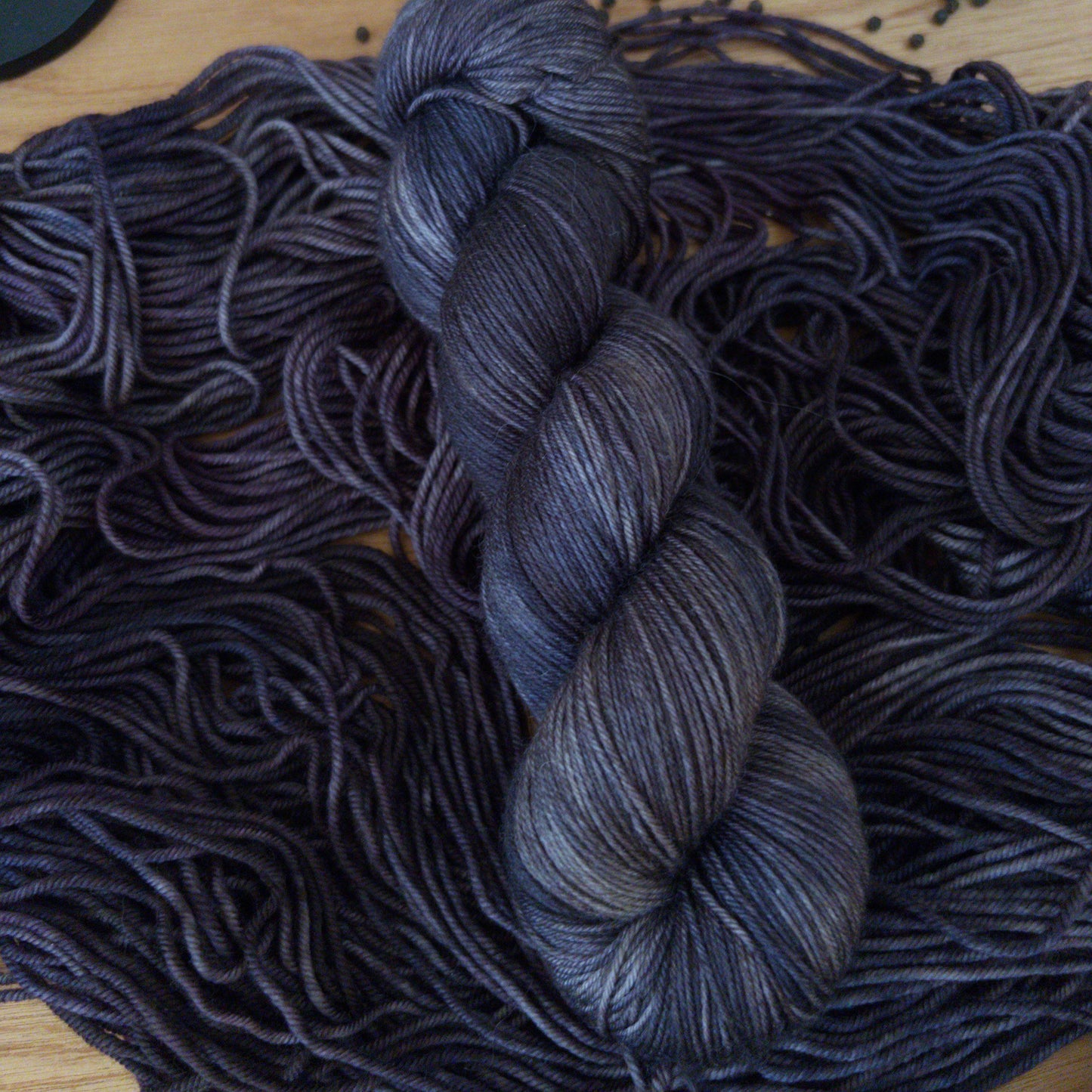 Charcoal gray skein of yarn on a wooden surface with other yarn and pumpkins.
