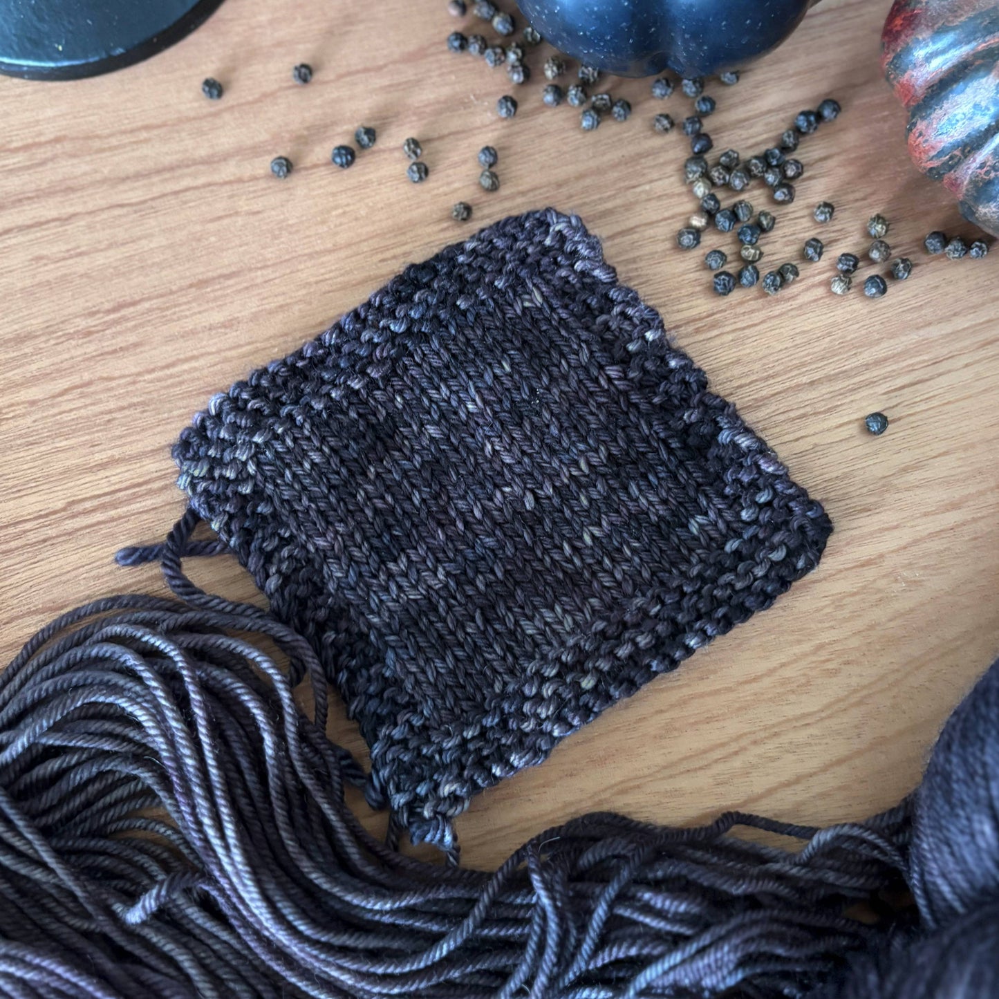 Knitted dark gray square with yarn and decorative elements on a wooden surface