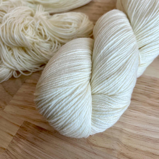 A skein of sock weight white yarn against a wood background.