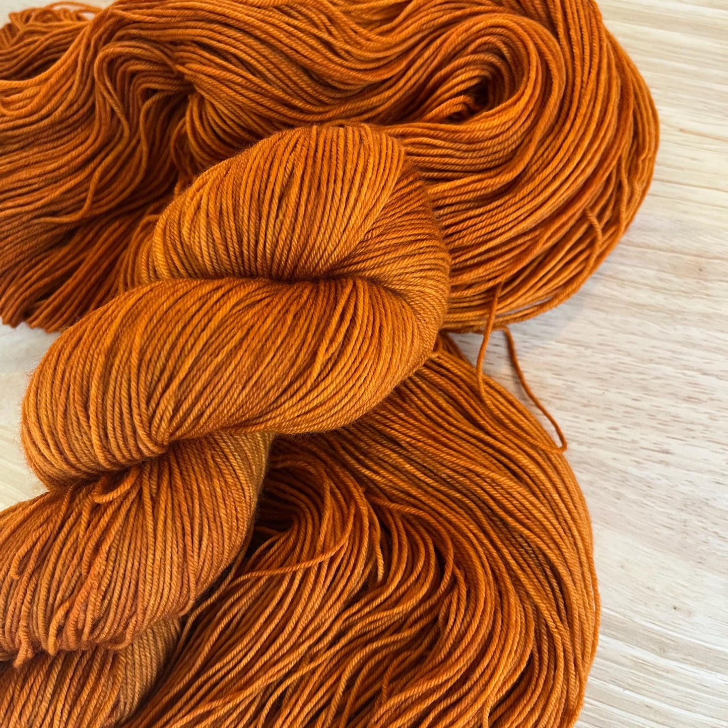 Warm rust orange hand dyed wool yarn arranged in a skein.