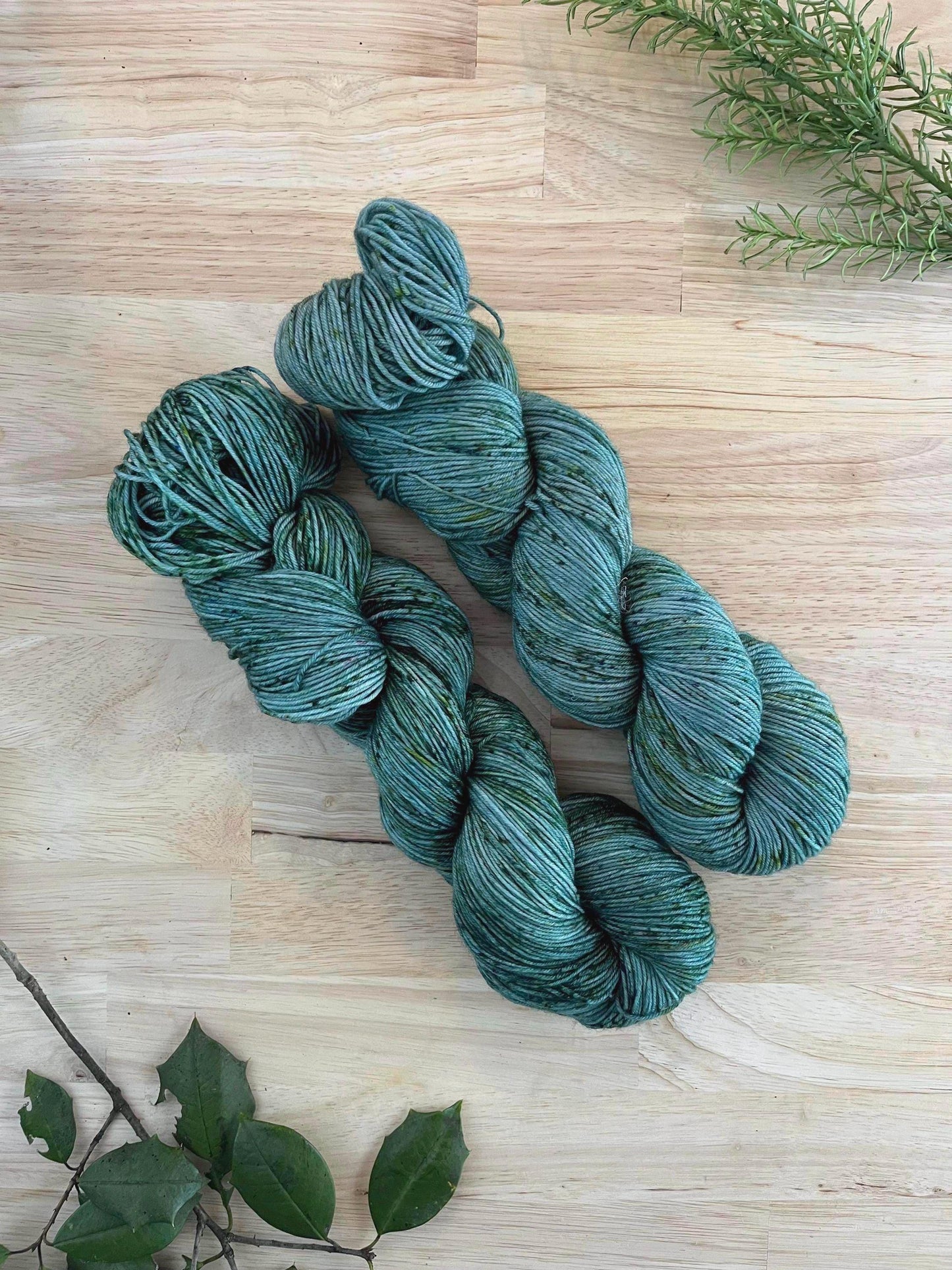 Two skeins of hand dyed gray green yarn with green speckles.