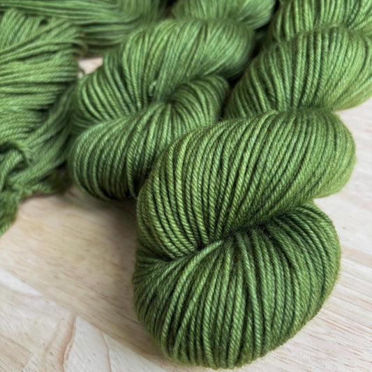 Skeins of dark warm green yarn on a wood backdrop.