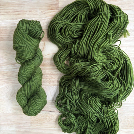 A skein of hand dyed warm green yarn arranged on a wood background.