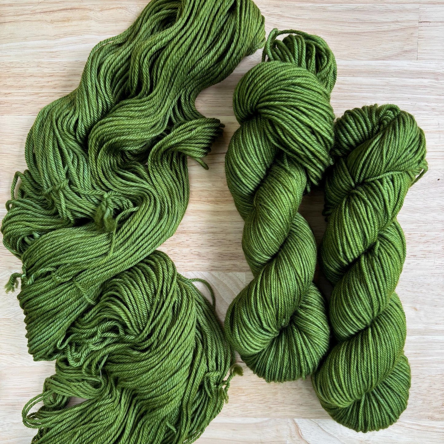 Skeins of hand dyed avocado green yarn against a wood background.