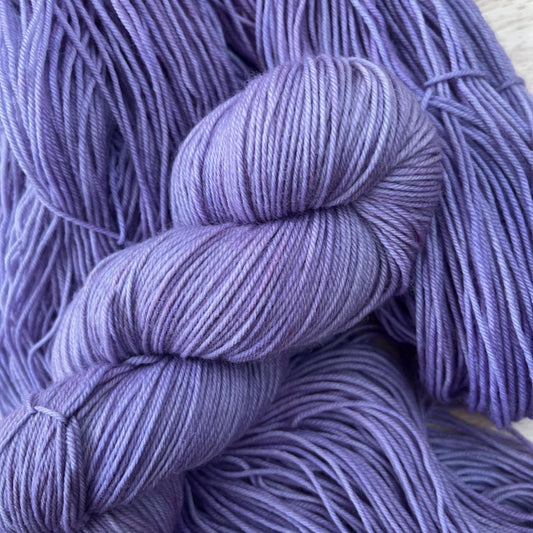 A skein of hand dyed purple yarn arranged with yarn behind it.