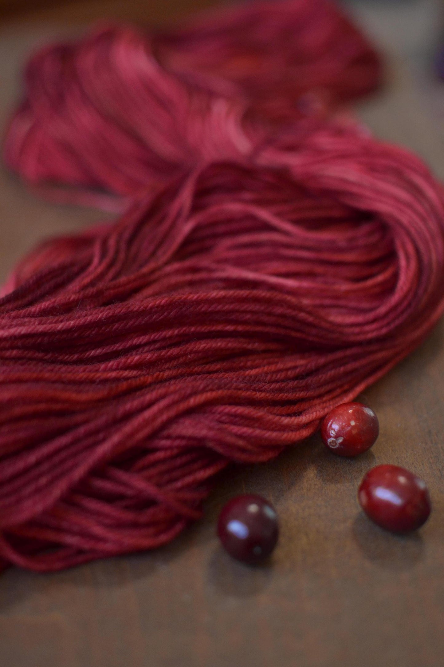 Dark red yarn spread on a dark wood backdrop with cranberries placed around.
