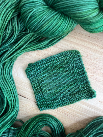 A knit swatch of hand dyed variegated jade green wool yarn.