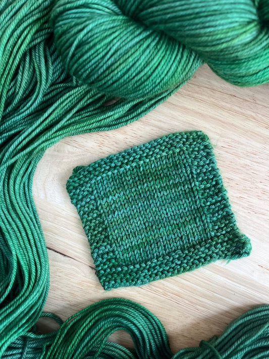 A knit swatch of hand dyed variegated jade green wool yarn.