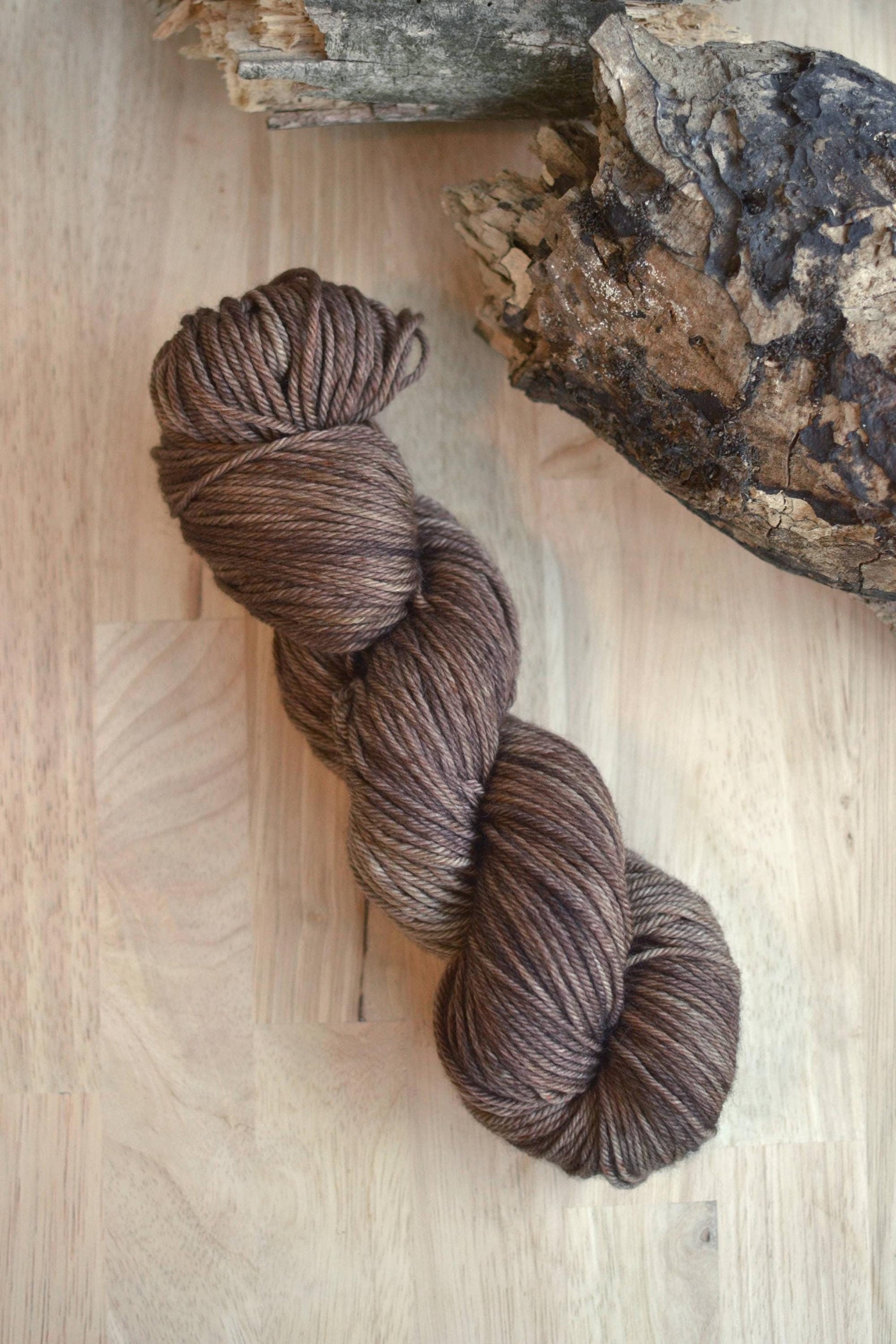 Neutral brown hand dyed merino wool yarn arranged on a wooden backdrop.