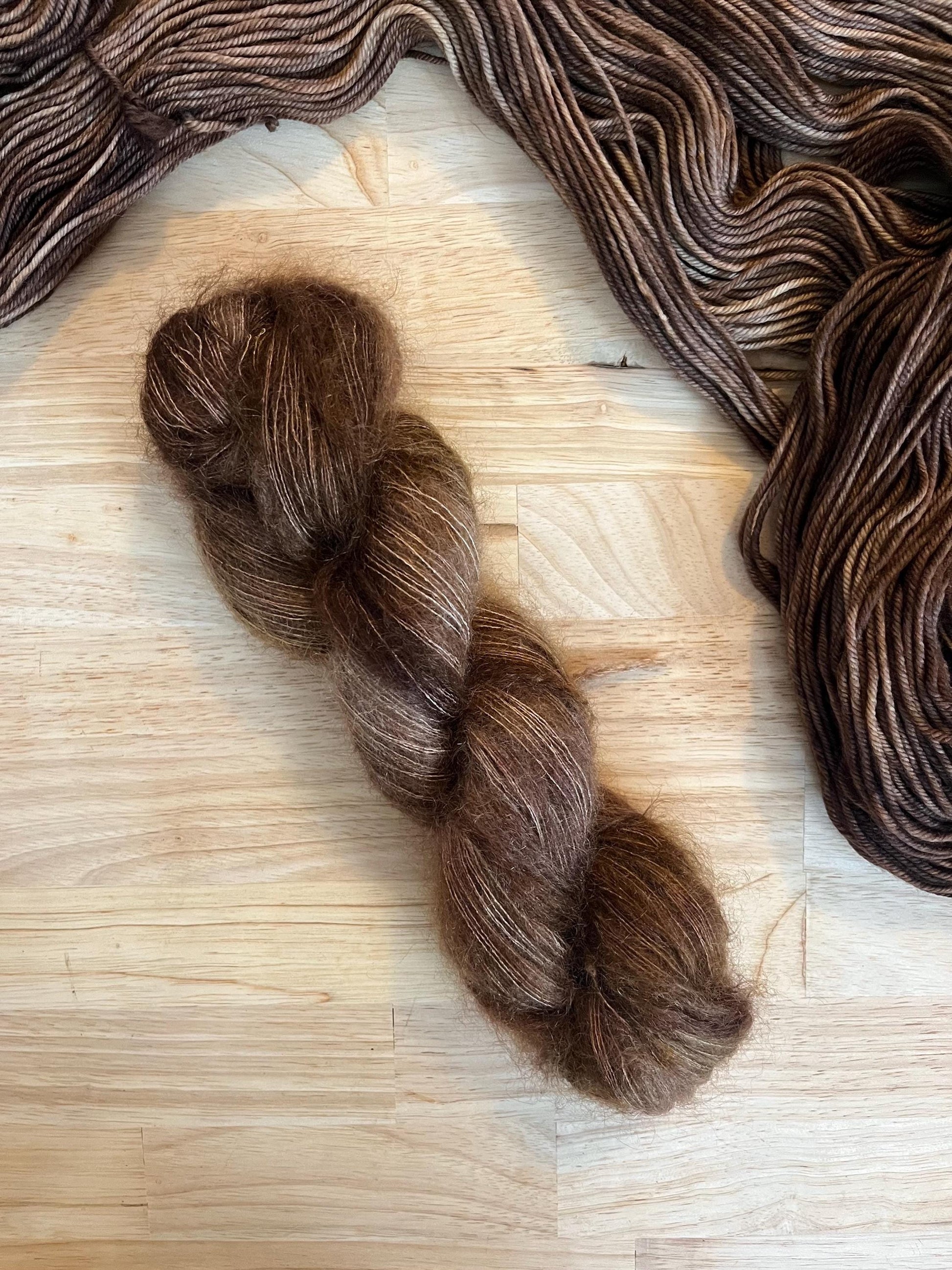 Hand dyed variegated neutral brown mohair silk yarn arranged on a wooden backdrop.