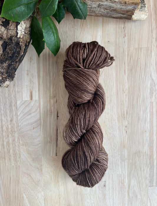 Hand dyed variegated neutral brown wool yarn arranged on a wooden backdrop.