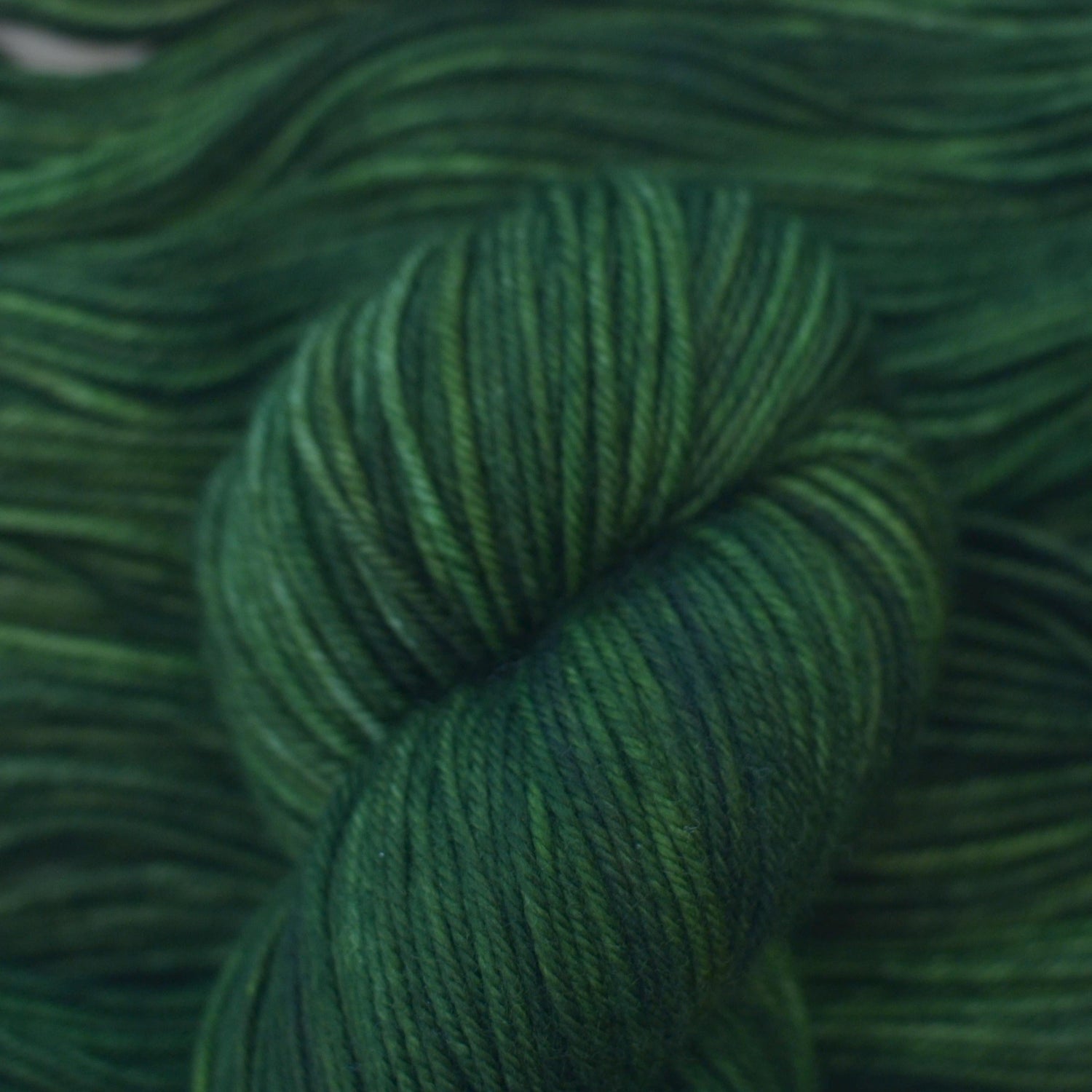 Skein of hand dyed variegated green merino yarn.