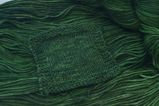 A knit swatch of hand dyed variegated green merino wool yarn.