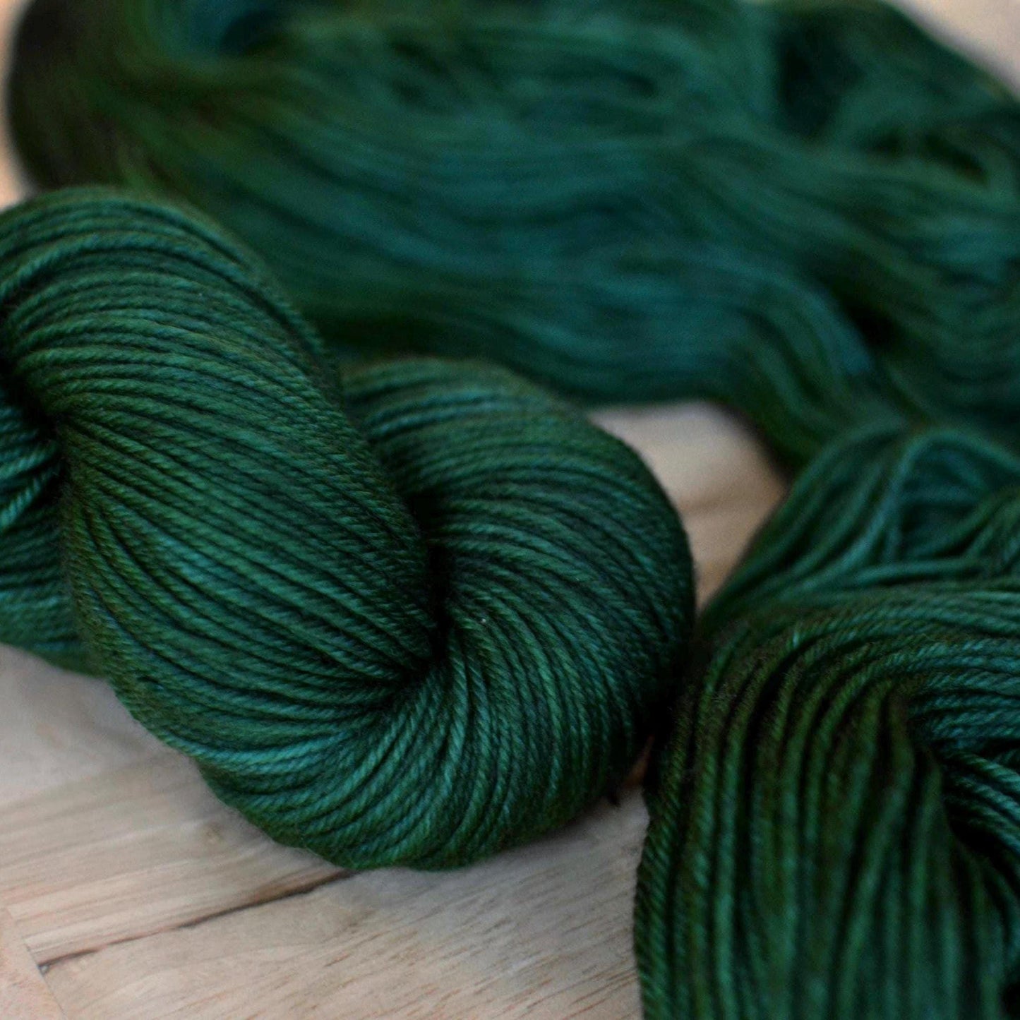 Skeins of hand dyed dark forest green merino wool yarn.