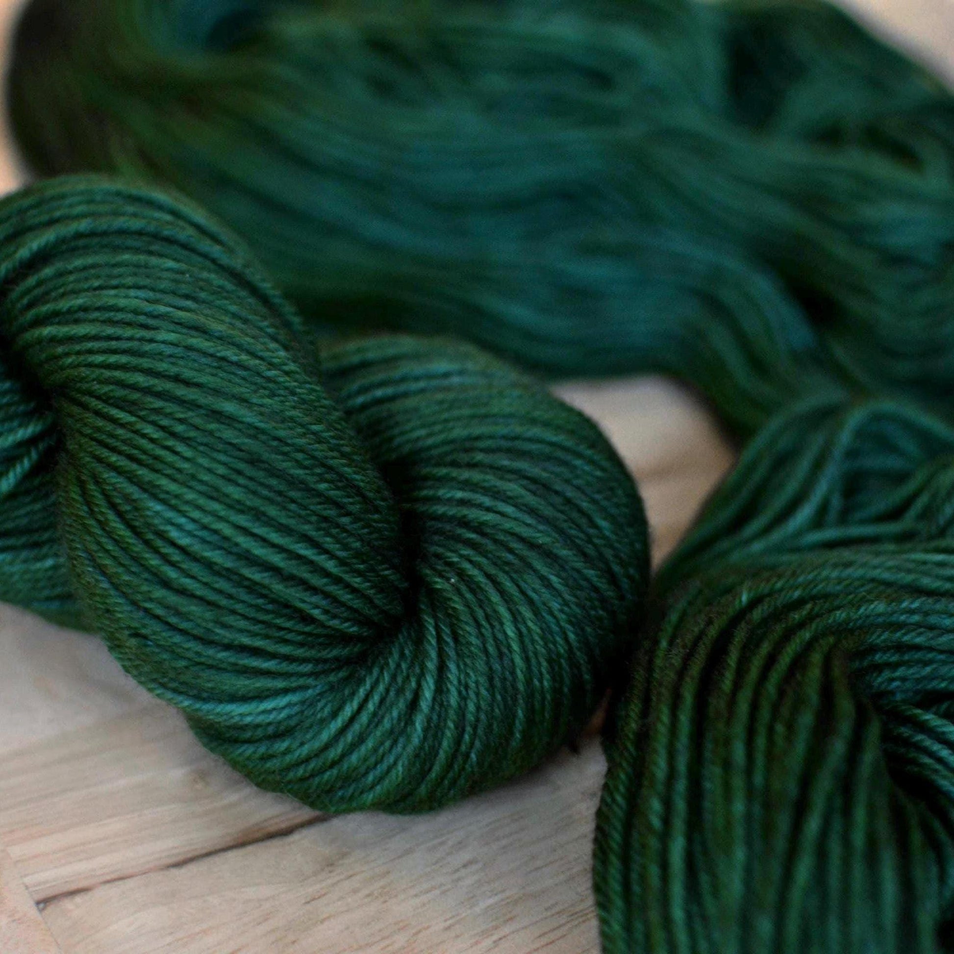 Skeins of hand dyed dark forest green merino wool yarn.