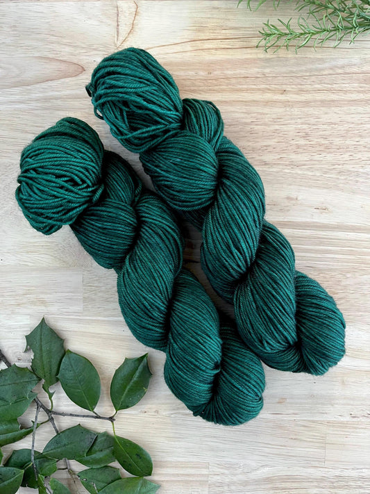 Skeins of hand dyed dark forest green merino wool yarn.