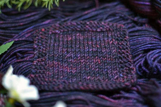 A knit swatch of hand dyed variegated purple and dark red merino wool yarn.