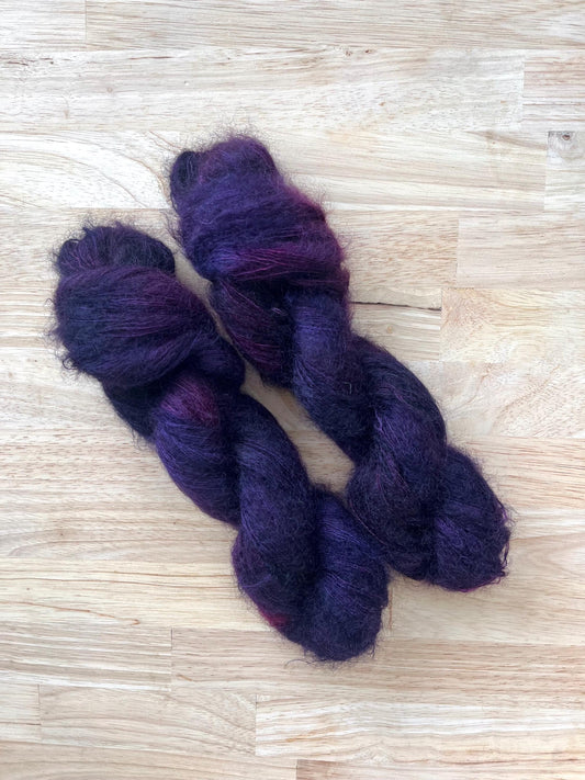 Two skeins of hand dyed variegated purple and dark red mohair silk lace yarn.