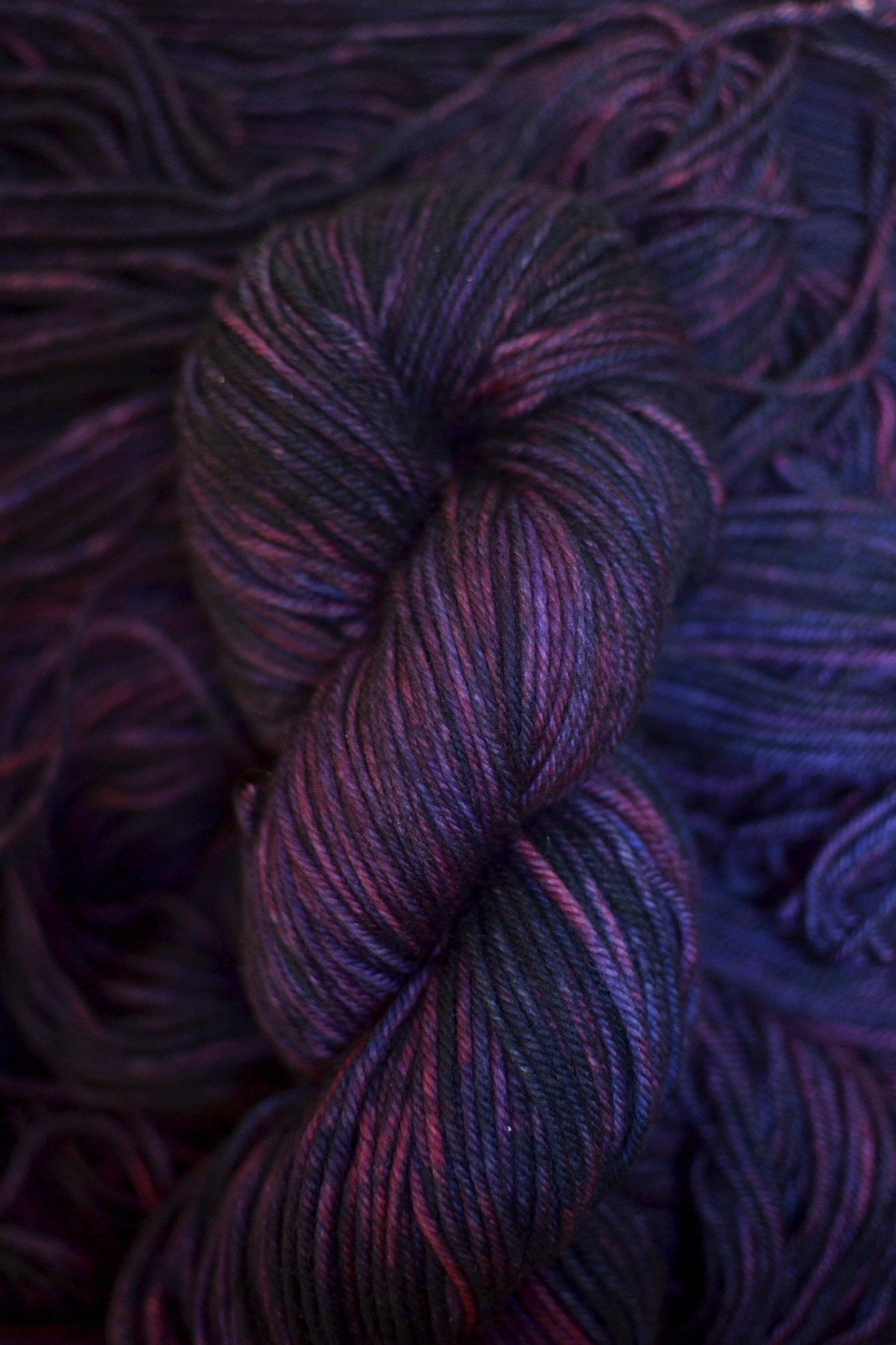 A DK weight skein of variegated purple and dark red merino wool yarn.