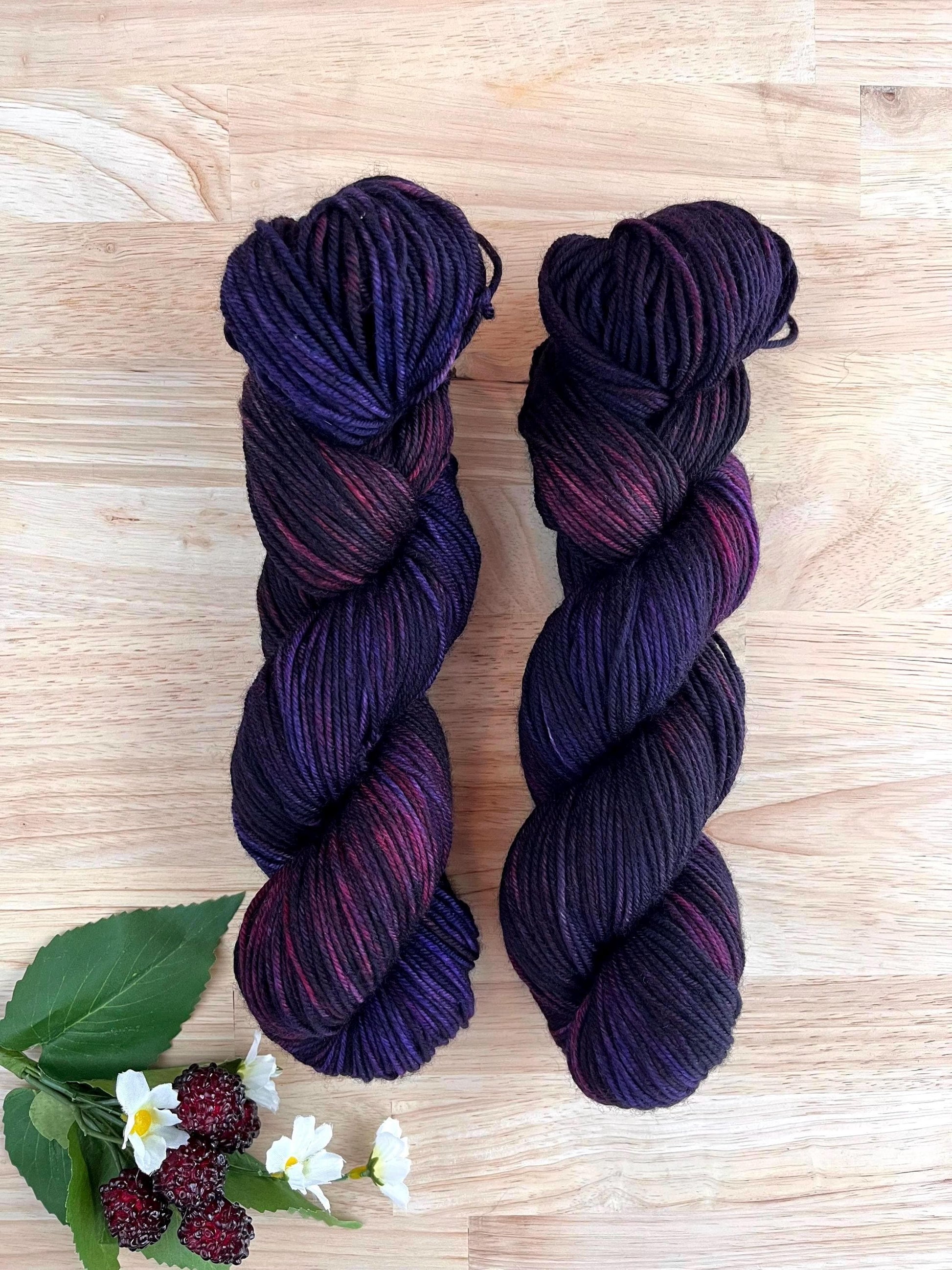 Skeins of DK weight hand dyed variegated purple and dark red merino wool yarn.