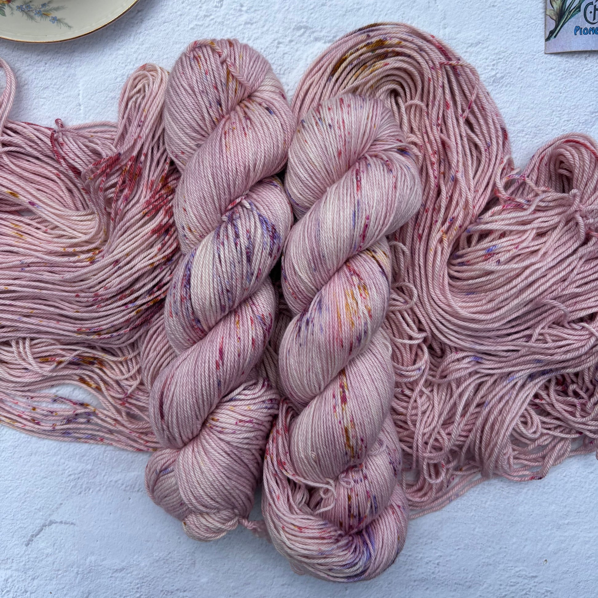 Two skeins of pink yarn on a light surface with a cup and lemon in the background.