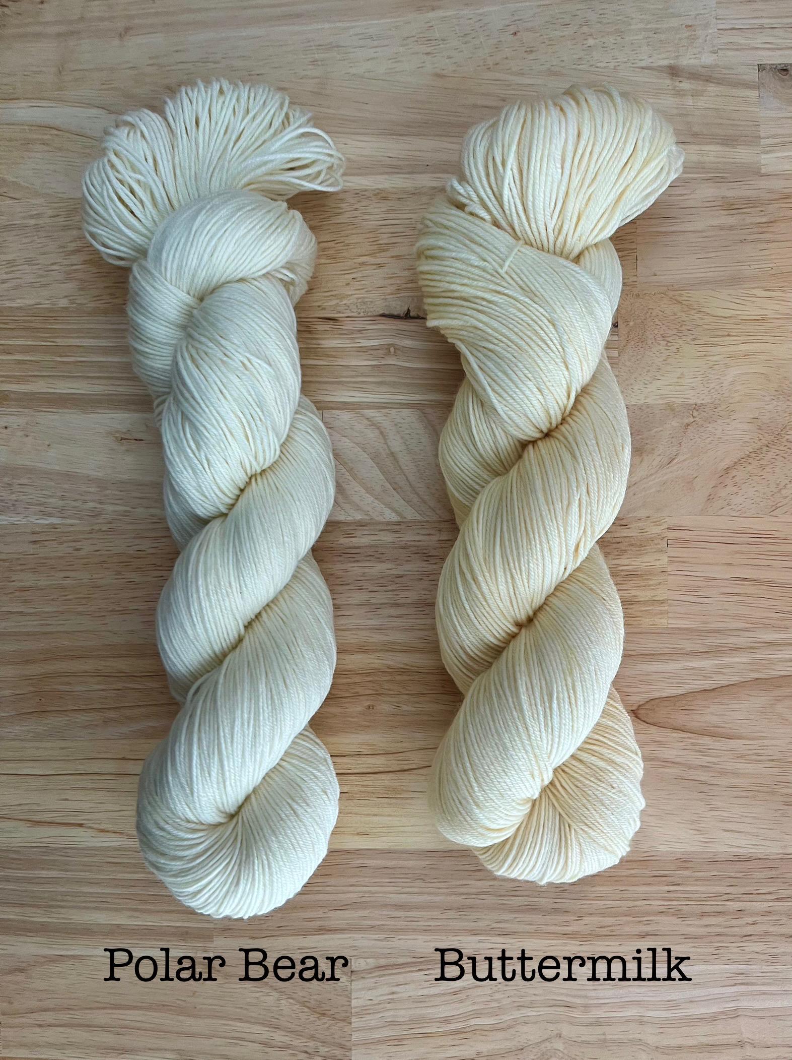 A skein of pure white yarn and a skein of hand dyed ivory cream yarn.