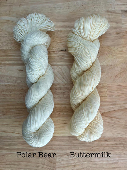 A skein of pure white yarn and a skein of hand dyed ivory cream yarn.