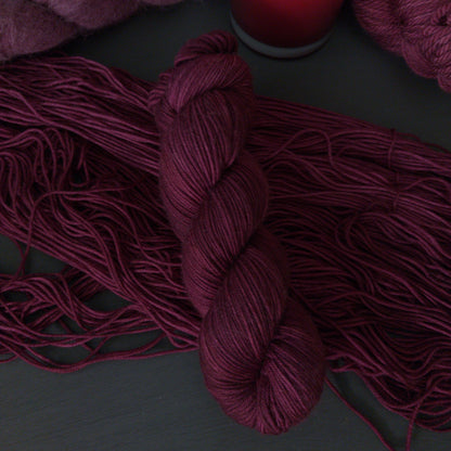 Burgundy yarn skeins with a lit red candle on a dark surface