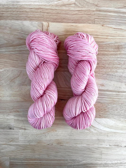 Skeins of tonal pale pink hand dyed merino yarn arranged against a wood background.